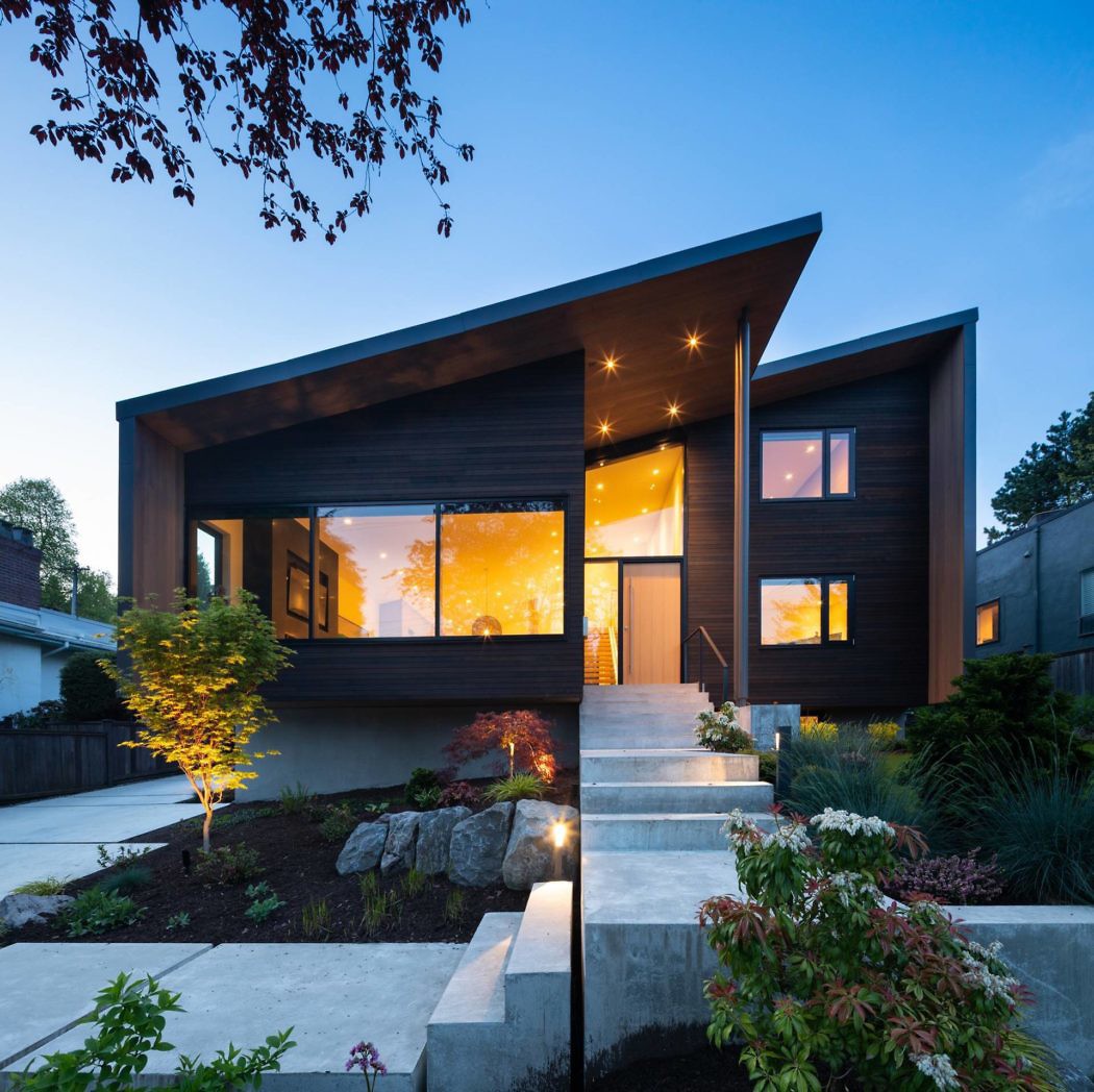 Modern house with large windows at dusk, exterior lights on.