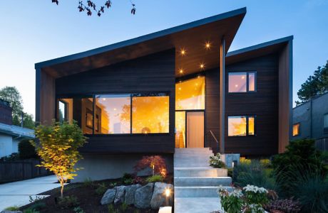 Modern house with large windows at dusk, exterior lights on.