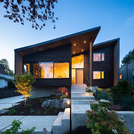 Modern house with large windows at dusk, exterior lights on.