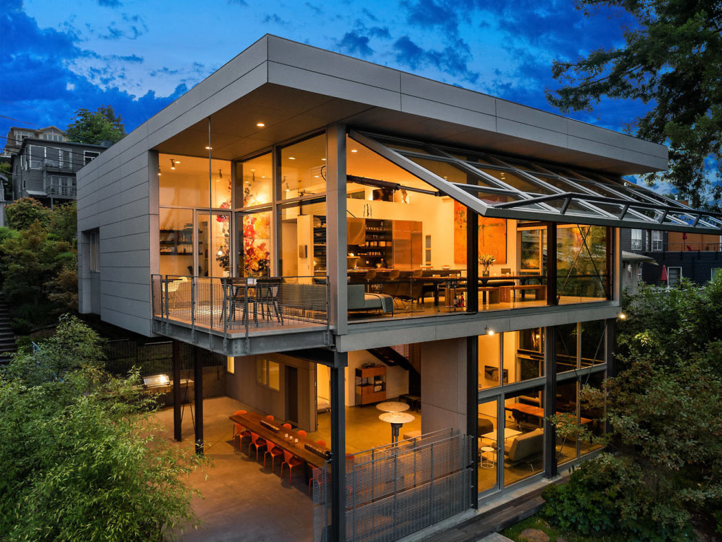 Contemporary home with glass walls at dusk, featuring a spacious balcony and glowing interior