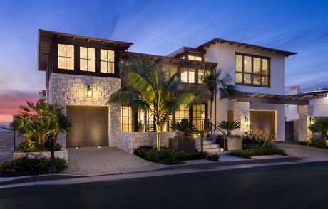 Modern two-story house with stone facade and palm trees at dusk.