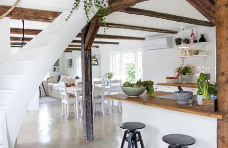 Modern rustic kitchen with white decor, exposed beams, and a spiral staircase.