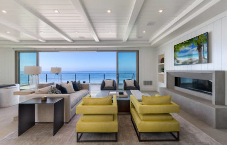 Modern living room with ocean view, green sofas, and a fireplace.