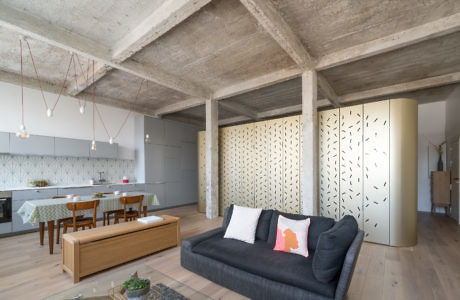 Modern apartment interior with exposed concrete beams, open-plan living and dining area.