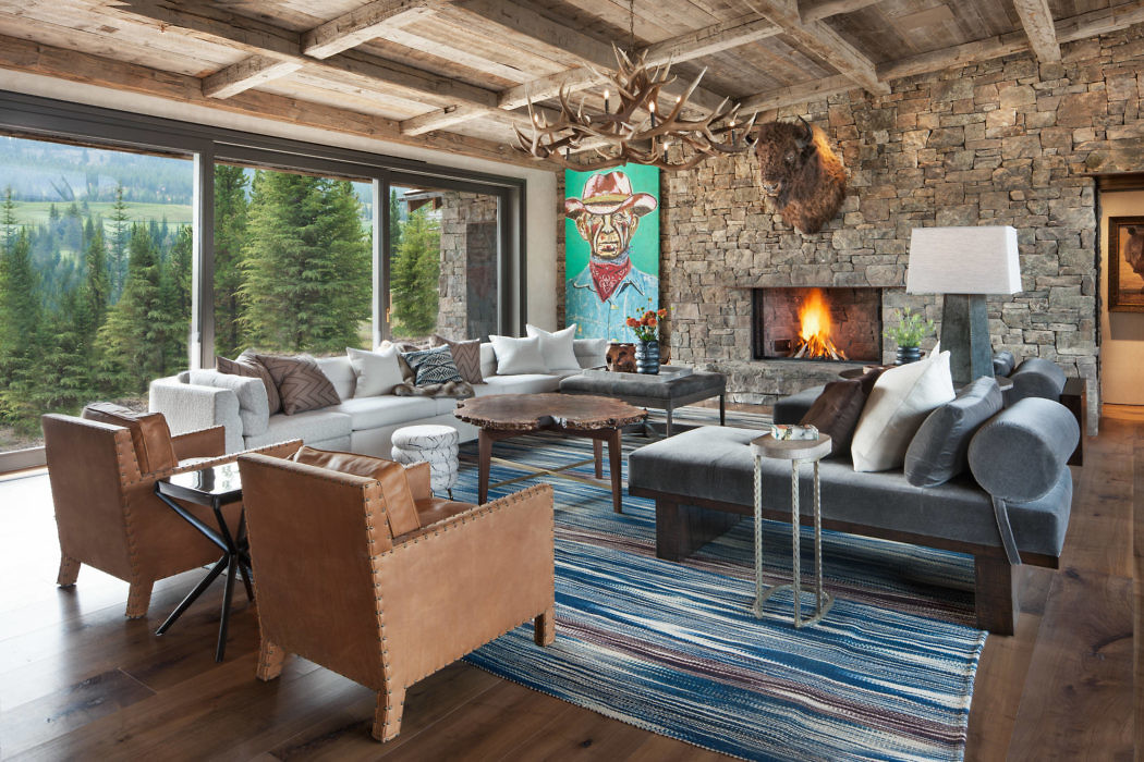 Rustic living room with a stone fireplace, large windows, and wooden beams