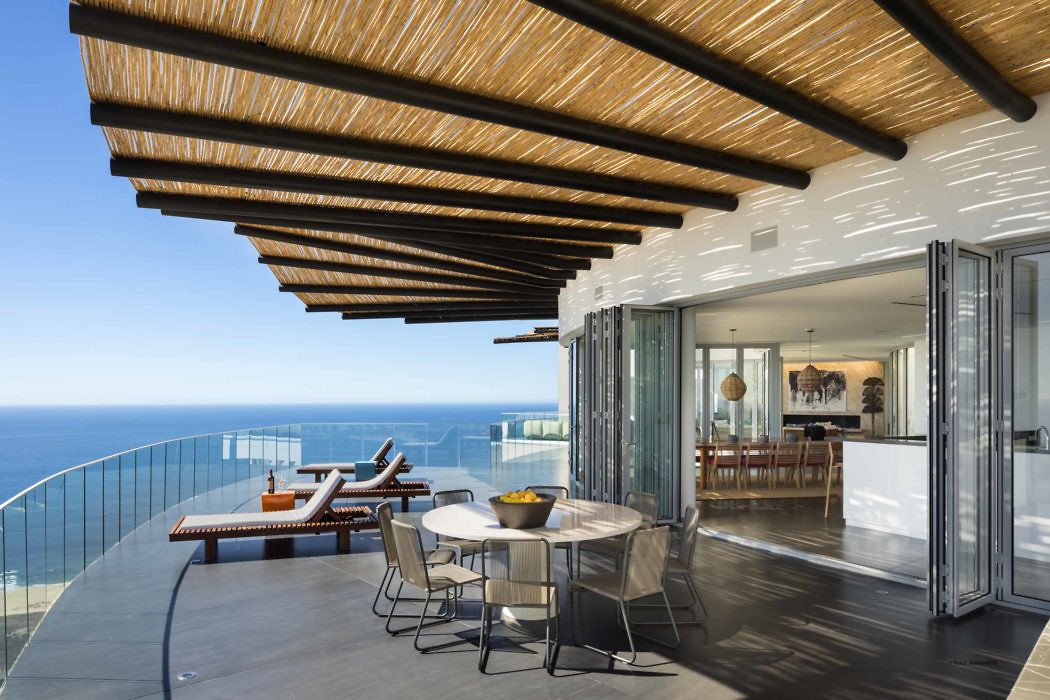 Oceanfront terrace with a slatted wooden overhang and glass balustrades.