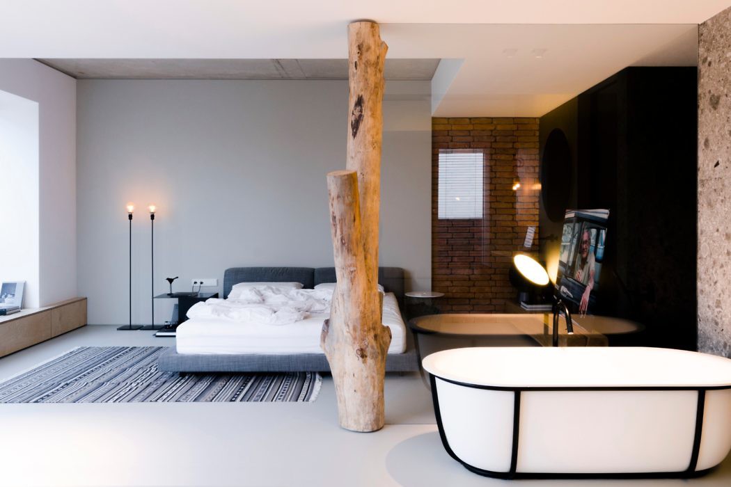 Modern bedroom with bed, freestanding bathtub, and contrasting rustic and sleek design