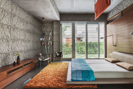 Modern bedroom with concrete and wood walls, large window, and colorful rug.