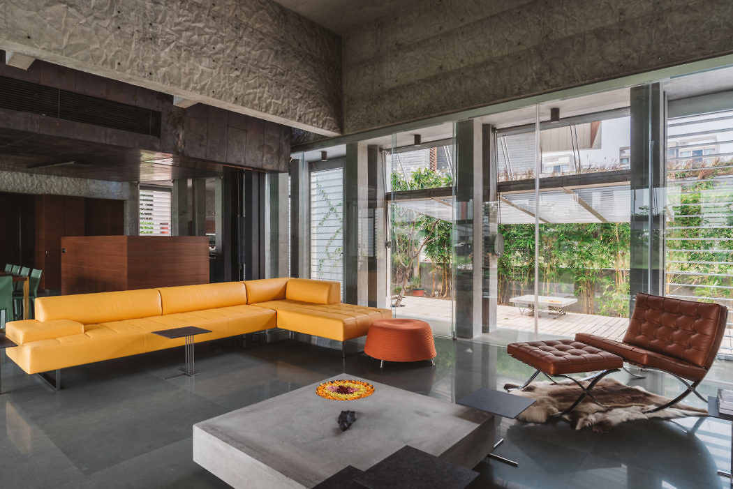 Modern living room with yellow sofa, concrete walls, and glass doors.