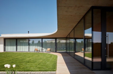 Curvilinear house with expansive glass walls and a shaded patio.