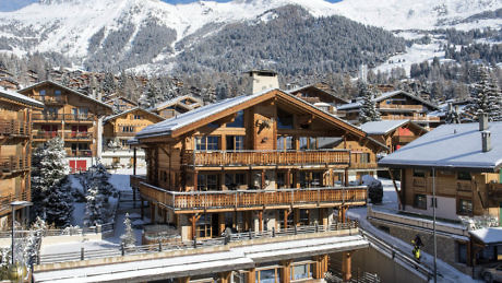 Alpine chalet with wooden balconies against snowy mountain backdrop.