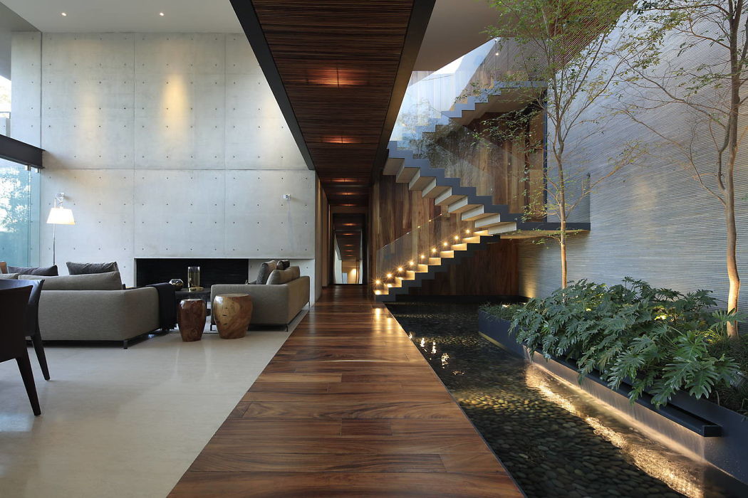 Modern indoor hallway with floating staircase, water feature, and lush greenery.