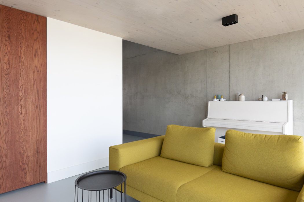 Contemporary living room with yellow sofa, concrete walls, and wood paneling.