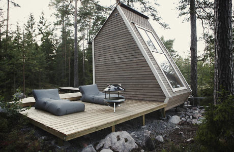 A-frame cabin with large window and wooden deck in a forest setting.