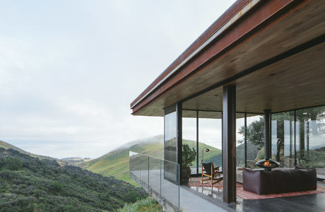 Modern house terrace with a glass facade overlooking green hills.