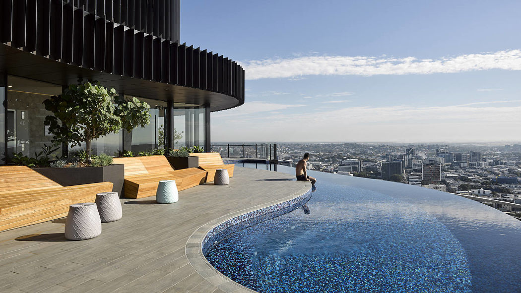 Rooftop infinity pool with wooden benches and city skyline view.