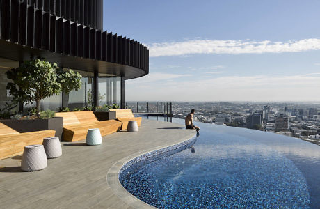 Rooftop infinity pool with wooden benches and city skyline view.