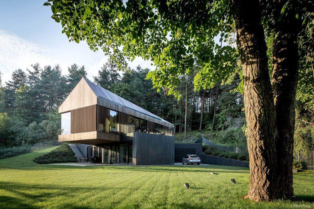 Contemporary two-story house with a pitched roof, surrounded by woodland.