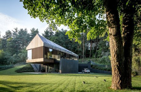 Contemporary two-story house with a pitched roof, surrounded by woodland.