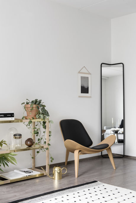 Modern minimalist room with a black chair, shelf, mirror, and decorative plants.