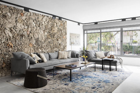 Modern living room with stone wall, grey sofa, and blue rug.