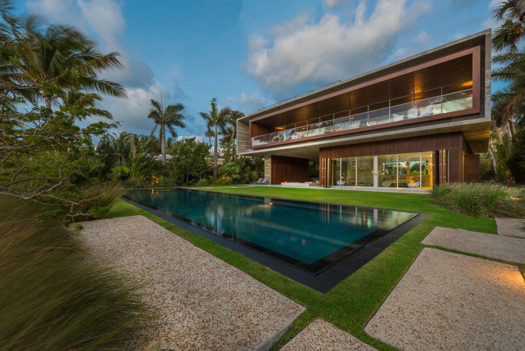 Contemporary house with expansive glass walls and an infinity pool amidst tropical landscaping.