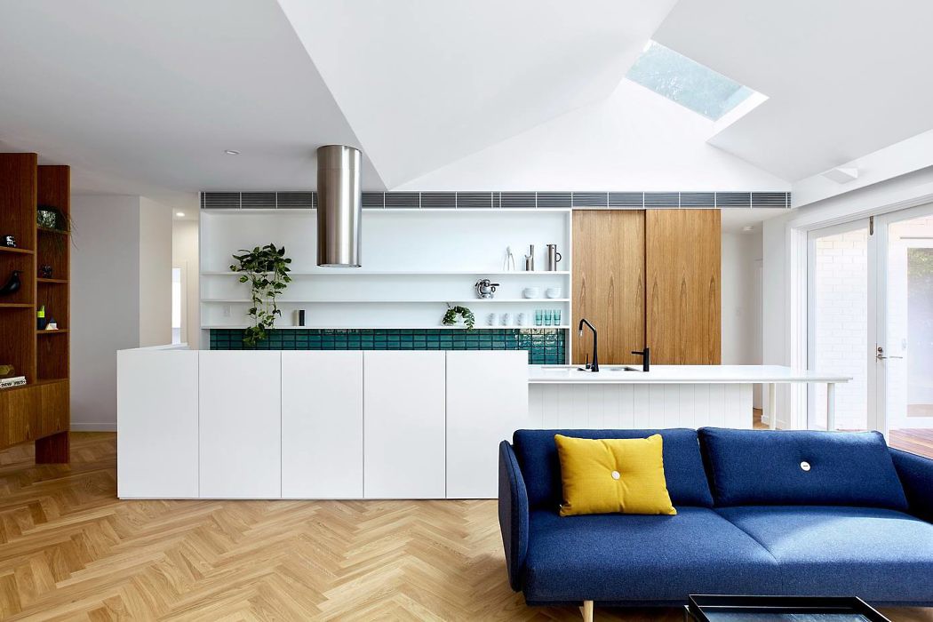 Modern kitchen with white cabinets and central island, adjacent to living area with blue sofa