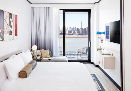 Sleek bedroom with city skyline view through balcony doors.