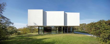 Minimalist white cubic house with glass lower level on a green lawn.