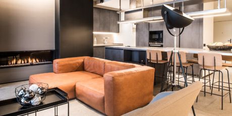 Contemporary living space with sleek kitchen, fireplace, and tan sectional sofa.