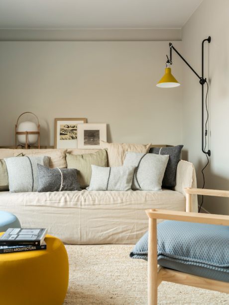 Cozy living room with beige couch, pillows, wall-mounted lamp, and yellow