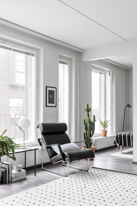 Modern living room with black chair, white walls, and large windows.