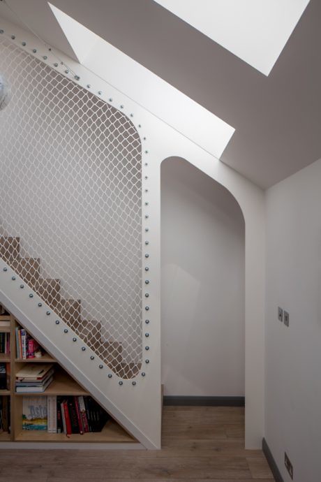 Modern stairwell with a white geometric railing and built-in bookshelf below.