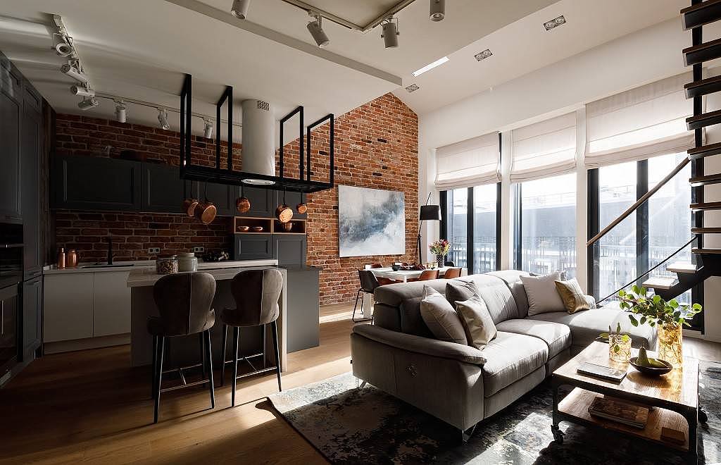 Modern loft living room with exposed brick, black kitchen, and staircase.