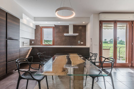 Modern dining room with glass table, chairs, and adjacent kitchen area.