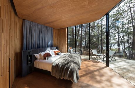 Wood-paneled bedroom with floor-to-ceiling glass wall overlooking a forest.