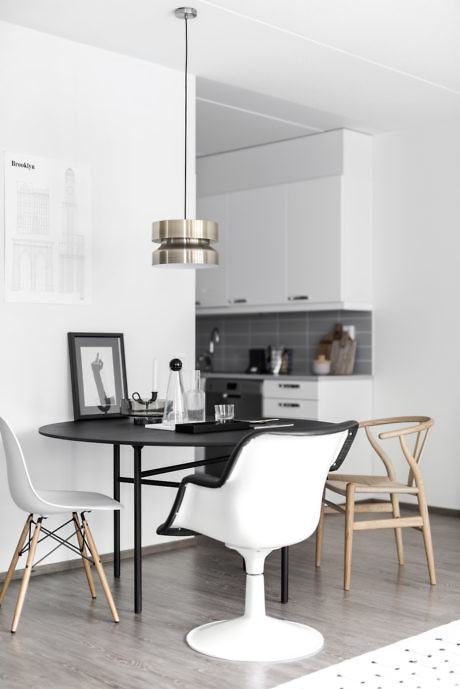 Modern kitchen with white cabinets, black dining table, designer chairs, and pendant light