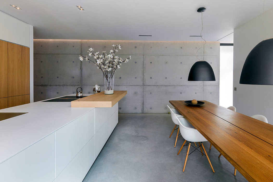Modern kitchen with a long wooden dining table, concrete walls, and pendant lights.