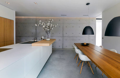 Modern kitchen with a long wooden dining table, concrete walls, and pendant lights.