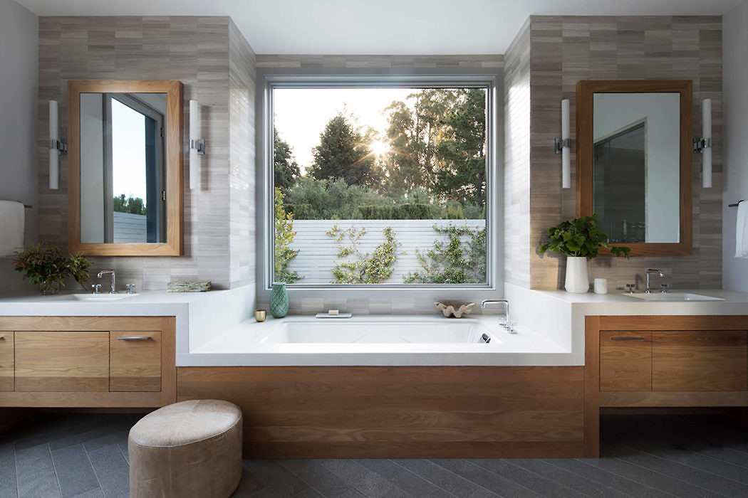 Modern bathroom with wooden cabinets and a large window above the bathtub.