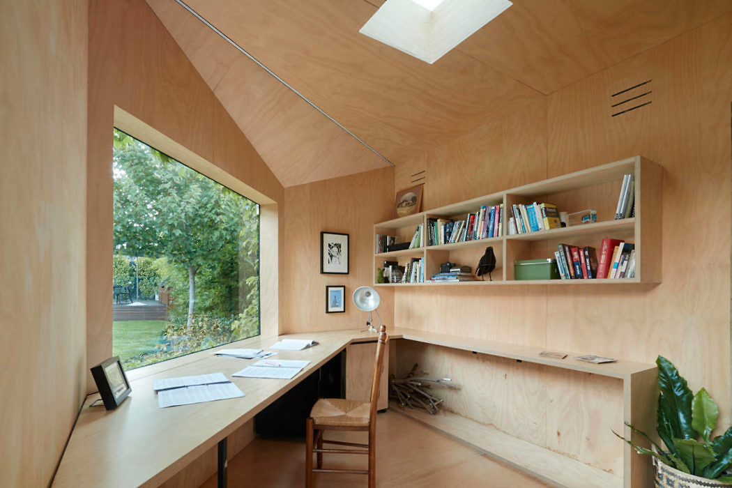 Modern home office with wooden walls, bookshelf, and a view of trees.