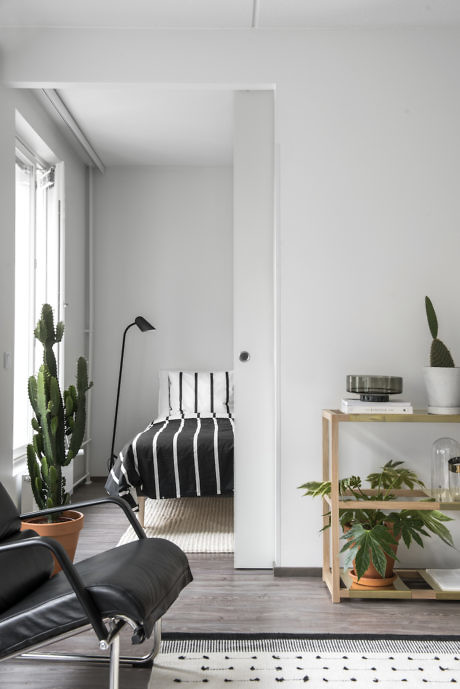 Minimalist interior with striped bedding, black chair, and green plants.
