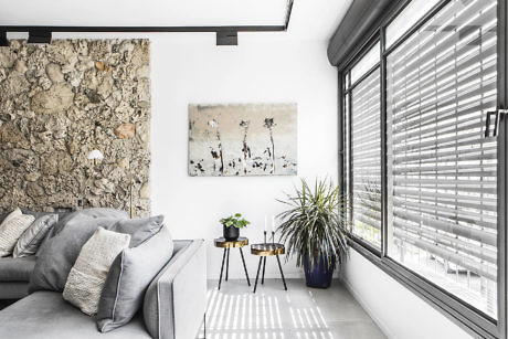 Modern living room with stone wall, sofa, artwork, and venetian blinds