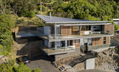 Modern hillside home with expansive glass walls and a metal roof.