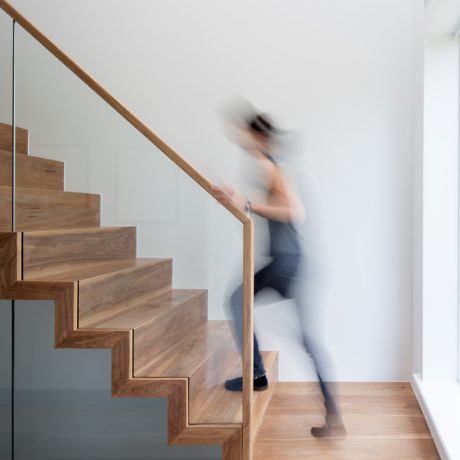 Person in motion ascending a modern wooden staircase with a glass balustrade.