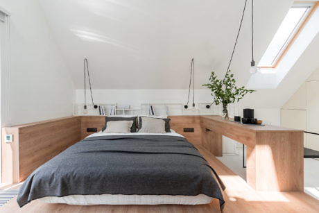 Minimalist attic bedroom with wooden furniture and skylights.