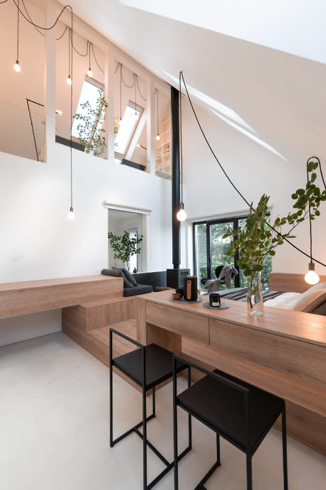 Minimalist interior with high ceiling, hanging lights, and wooden furnishings.