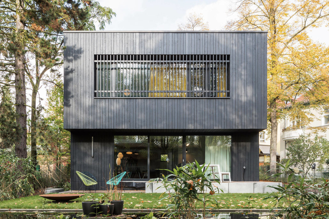 Contemporary two-story black timber house with large windows and a balcony.