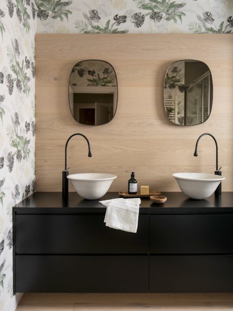 Contemporary bathroom with dual vessel sinks, black vanity, and floral wallpaper.
