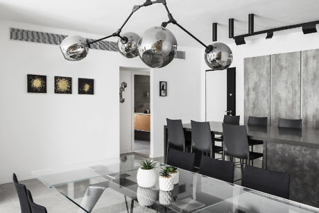 Modern dining room with a glass table, black chairs, and spherical pendant lights.
